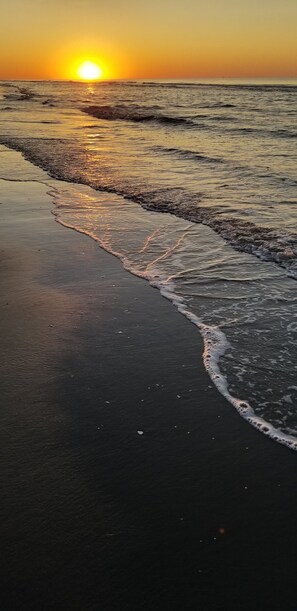 A beach at sunset with waves gently lapping onto the shore.