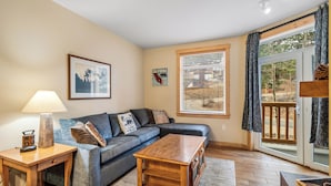 A living room with a sofa, coffee table, lamp, and a window with blinds. - Ski In-Ski Out Exclusive Lift Access Resort Condo at Mammoth Mountain Lakes CA (Mammoth Lakes)