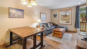 A living room with a wooden table, a sofa, a lamp, and a window with blinds. - Ski In-Ski Out Exclusive Lift Access Resort Condo at Mammoth Mountain Lakes CA (Mammoth Lakes)