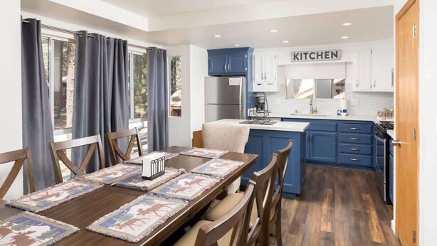 A modern kitchen with blue cabinets, a central island, and a dining area with a wooden table and chairs.