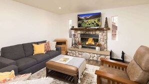 A living room with a stone fireplace, a sofa, a coffee table, and a television mounted above the fireplace.