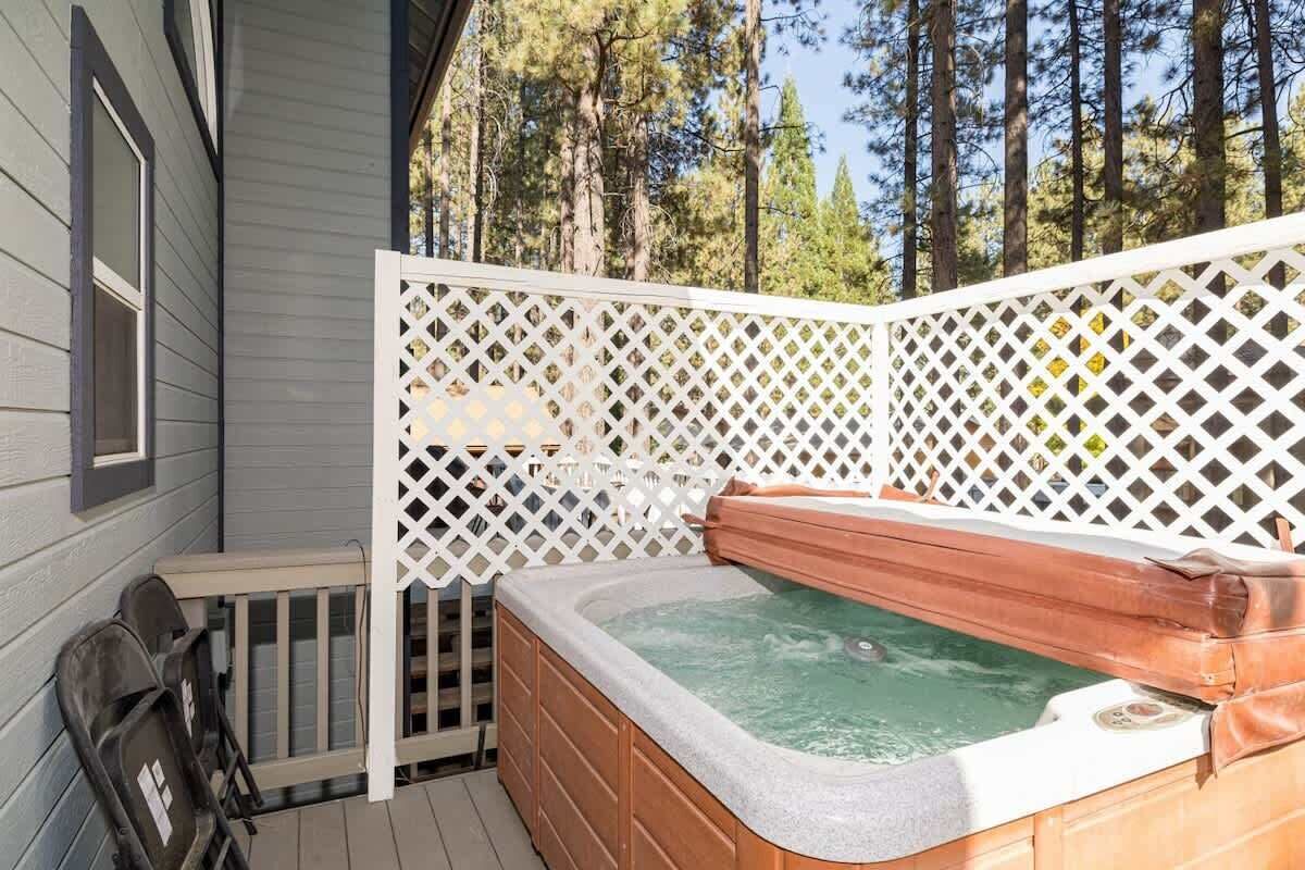A hot tub on a wooden deck with a white lattice fence, surrounded by trees.