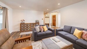 A modern living room with two grey sofas, a wooden coffee table, and a small side table. A wooden cabinet with decorative items is against the wall.