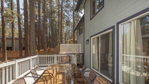A deck with a glass-top table and chairs, surrounded by tall trees.
