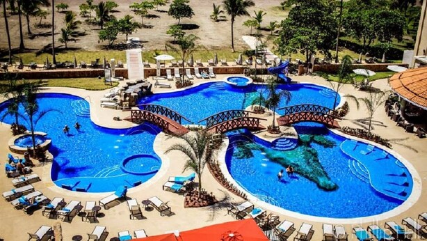 A resort with multiple interconnected swimming pools, lounge areas, and a beach view.