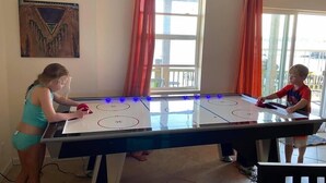 A room with a large ice hockey table, a painting on the wall, and a window with curtains.