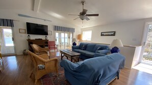 A spacious living room with a blue sofa, wicker chairs, a wooden coffee table, and a ceiling fan.