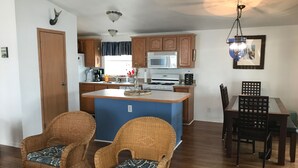 A compact kitchen with wooden cabinets, a central island, and a dining area with wicker chairs.