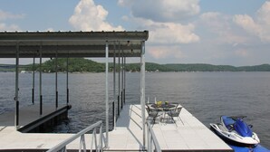 A dock with a covered seating area, a jet ski, and a view of a lake with distant hills.