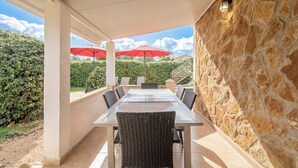 Eine Terrasse im Freien mit Tisch, Stühlen, roten Sonnenschirmen und Steinmauern.