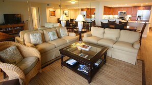 Una sala de estar con un sofá, sillones, una mesa de centro de vidrio y un televisor.