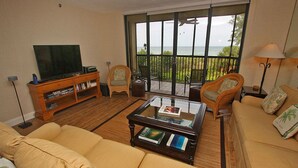 Una sala de estar con un sofá, una mesa de centro, un televisor y un balcón con vistas al océano.