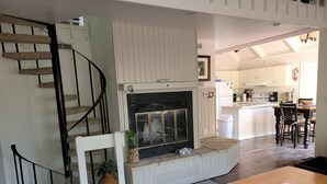 A living room with a fireplace, wooden staircase, and a kitchen area in the background. - 2 Bedroom + Loft, 2 bath house in The Galena Territory. (Galena)