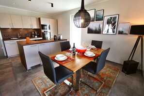 A modern kitchen with white cabinets, a wooden island, and a dining area with a wooden table and black chairs.