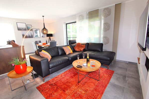 A modern living room with a black leather sofa, a wooden coffee table, and a red patterned rug.