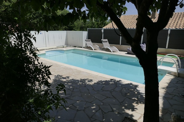 A swimming pool with lounge chairs, a stone patio, and a white fence.