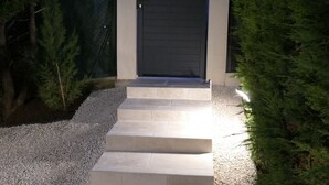A pathway leading to a dark-colored door, flanked by a small tree and a hedge, with steps and gravel on either side. - In the heart of the Luberon Luxury apartment with private heated pool in a quiet  (Reillanne)