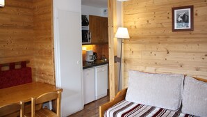 Una habitació acollidora amb una paret de fusta, un llit amb roba de llit a ratlles, una taula de fusta i una cuineta de fons.