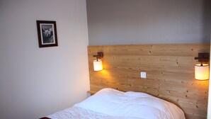 Un llit ben fet amb un panell frontal de fusta, dues làmpades penjades a la paret i una imatge emmarcada.