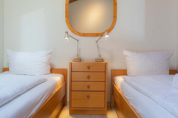 A bedroom with two beds, a wooden dresser, and a mirror above the dresser.