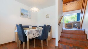 A dining area with a table set for two, a clock on the wall, and a staircase leading to an outdoor seating area.