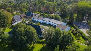 An aerial view of a residential area with a row of houses, green lawns, and a large building with a flat roof.
