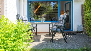 A patio with a table and two chairs, a window with a blue frame, and a white brick wall.