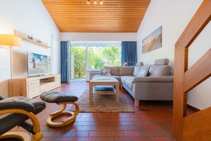 A modern living room with a wooden ceiling, a sofa, a coffee table, and a TV on a wooden stand.