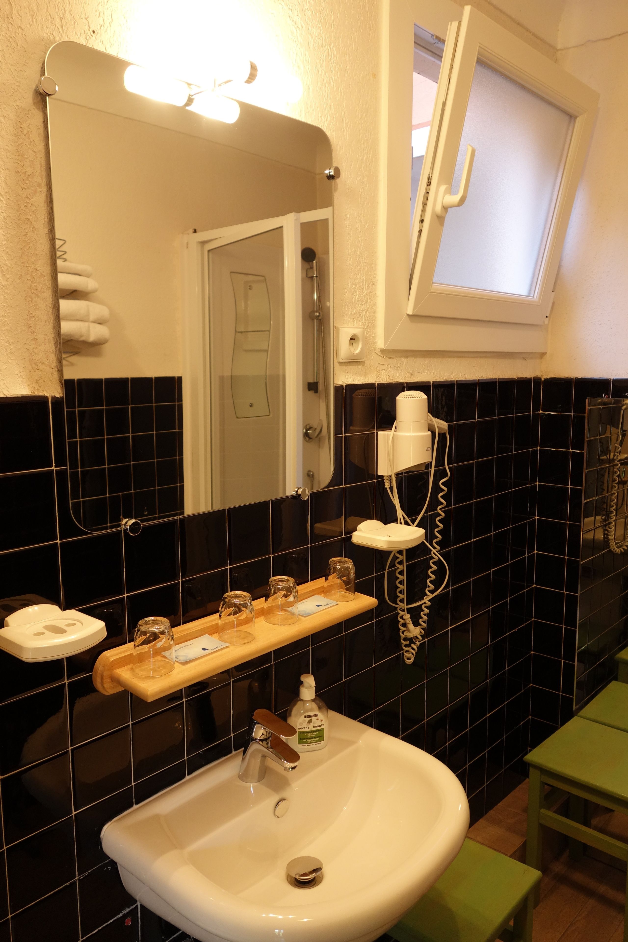 Une salle de bain avec un lavabo blanc, un miroir, un sèche-cheveux et un tabouret vert.