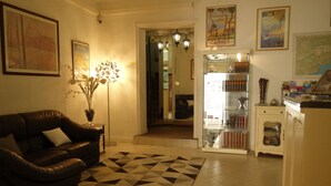 A living room with a leather sofa, a patterned rug, a vase with flowers, and a bookshelf. - Hotel le Préjoly (Saint-Vallier-de-Thiey)
