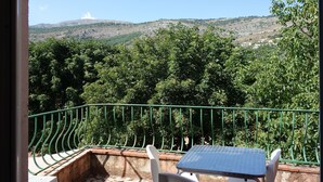 A balcony with a table and chairs, overlooking a hillside with trees and a distant building. - Hotel le Préjoly (Saint-Vallier-de-Thiey)