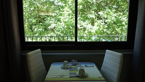A dining area with a table set for two, a window with a view of trees, and a striped tablecloth. - Hotel le Préjoly (Saint-Vallier-de-Thiey)