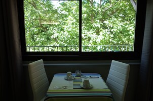 Un comedor con una mesa para dos, una ventana con vistas a árboles y un mantel a rayas.