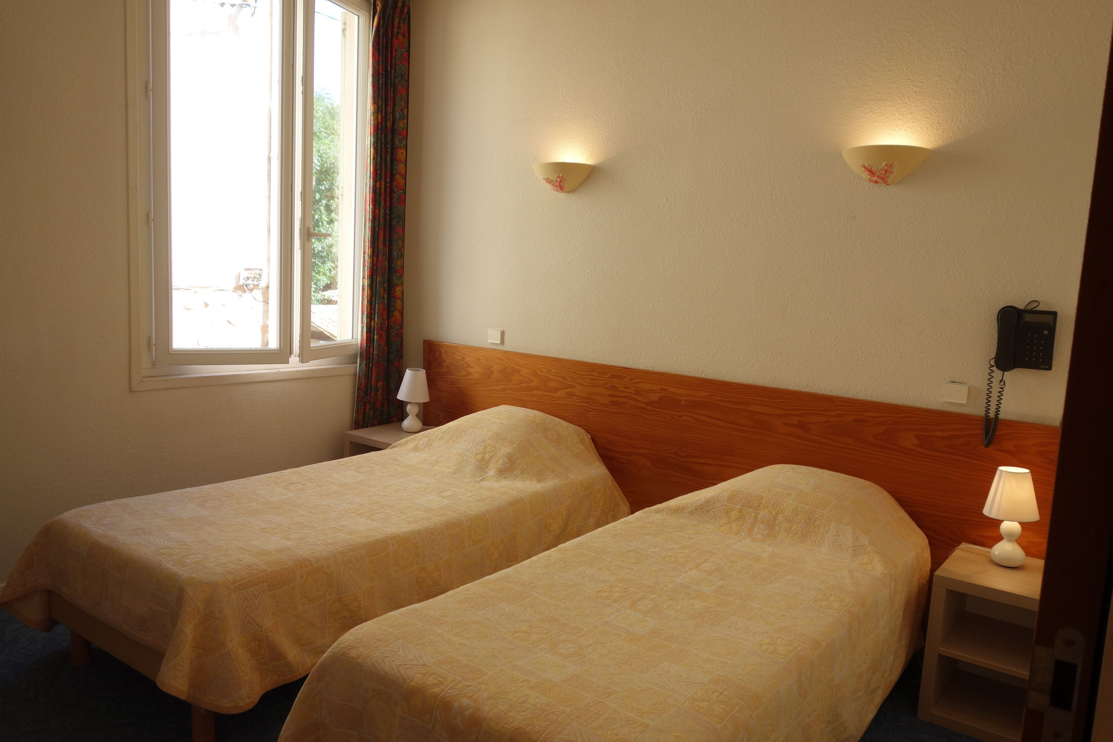 A hotel room with two single beds, a wooden headboard, bedside lamps, a telephone, and a window with curtains.