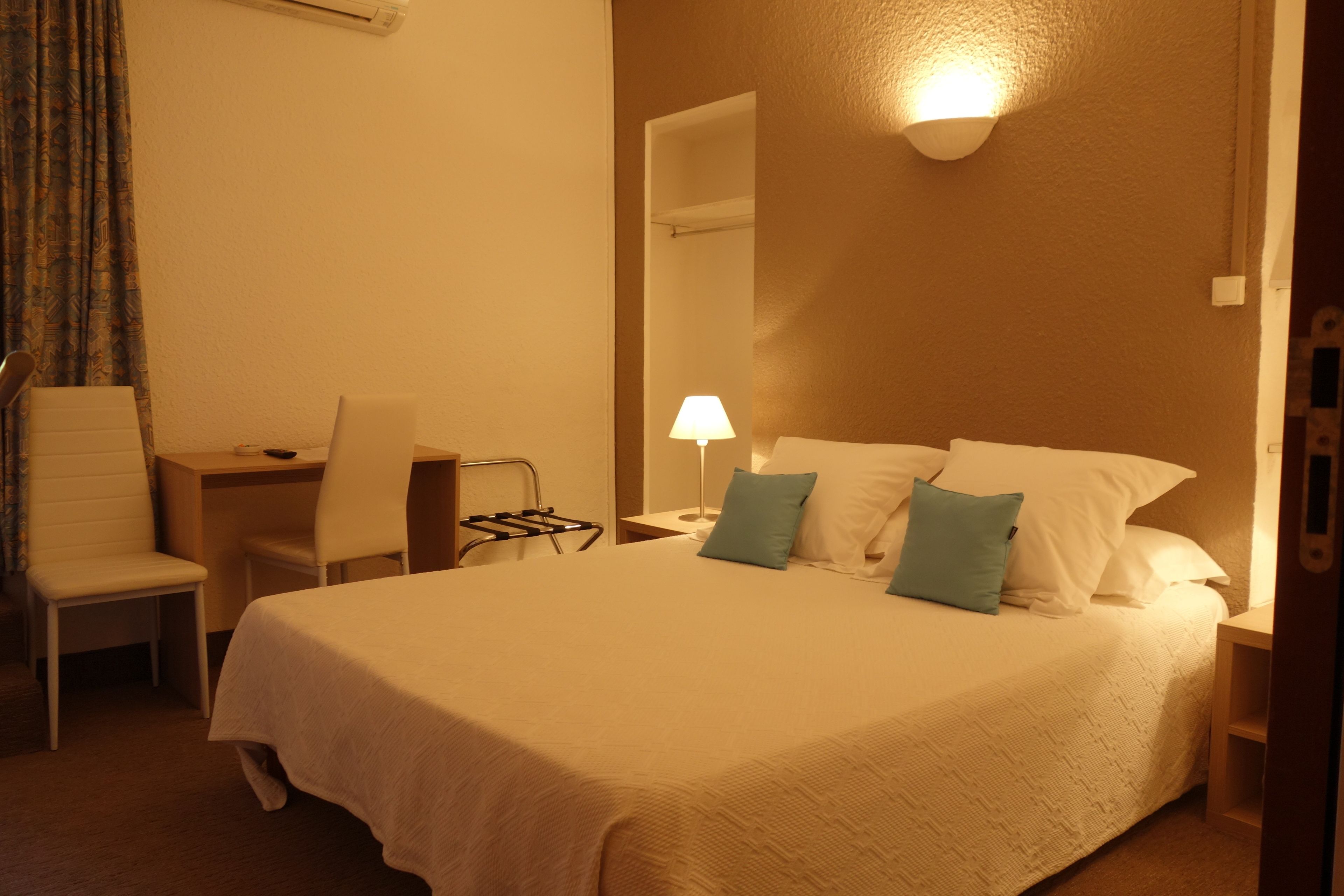 A hotel room with a bed, a desk, a chair, a lamp, and a mirror.