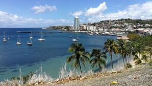 Un pueblo costero con un puerto deportivo, aguas azules cristalinas y un edificio destacado al fondo.