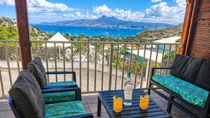 Un balcón con vistas al mar, dos sillas, una mesa y dos vasos de jugo de naranja.