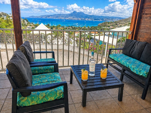 A balcony with a view of the sea, two chairs, a table, and two glasses of orange juice. - Les Trois Ilets: T2 Balisier with panoramic view of Fort de France bay (Les Trois-Îlets)