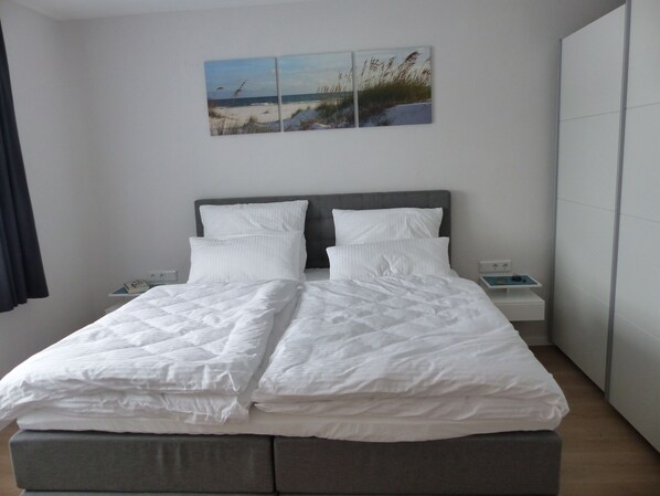 A neatly made bed with white linens, a grey headboard, and a bedside table with a lamp. - Comfort apartment, balcony, quiet, central location, apartments Flora (Bad Windsheim)