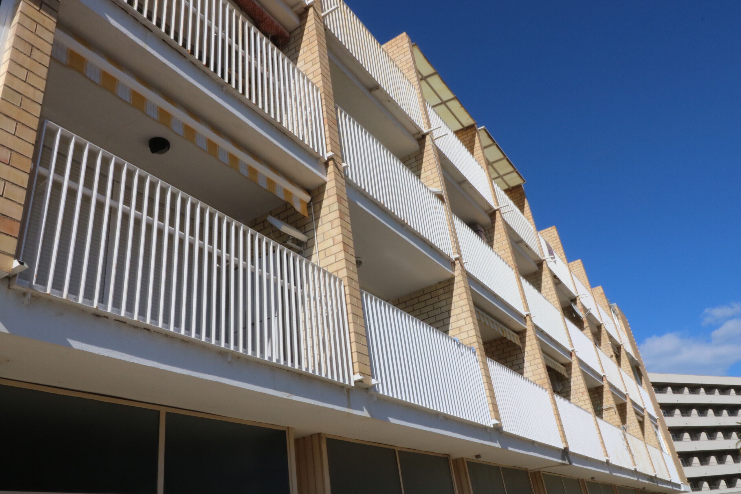 Un immeuble à plusieurs étages, doté de balcons et de fenêtres, avec un ciel bleu dégagé.