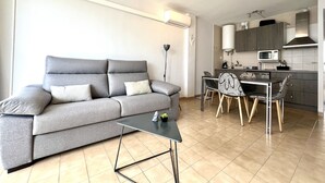 A modern living room with a grey sofa, a small coffee table, and a dining area with chairs and a table.