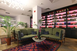 A modern lounge area with a green sofa, a coffee table, and a bookshelf filled with books. -  Hotel Europe (Tbilisi)