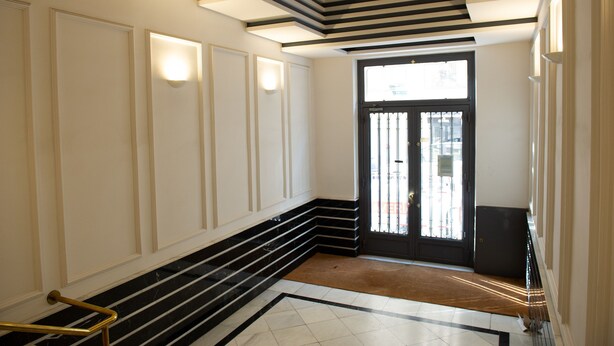 A hallway with a black and white tiled floor, a black door with a window, and a brown mat at the entrance. - Glorieta de Bilbao Madrid Centro (Madrid)