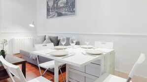 A dining area with a white table set for four, a gray sofa, and a framed cityscape picture on the wall. - Glorieta de Bilbao Madrid Centro (Madrid)