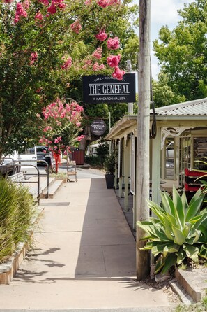 Straßenansicht mit einem Café namens 'The General' im Kangaroo Valley, mit Bürgersteig, parkten Autos und einem Gebäude mit einem Schild.