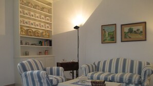 A living room with striped armchairs, a white coffee table, and a bookshelf filled with decorative plates and books.