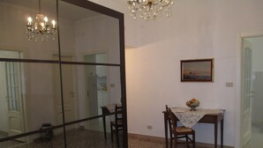 A dining area with a table, chairs, a chandelier, a painting, and a large mirror.