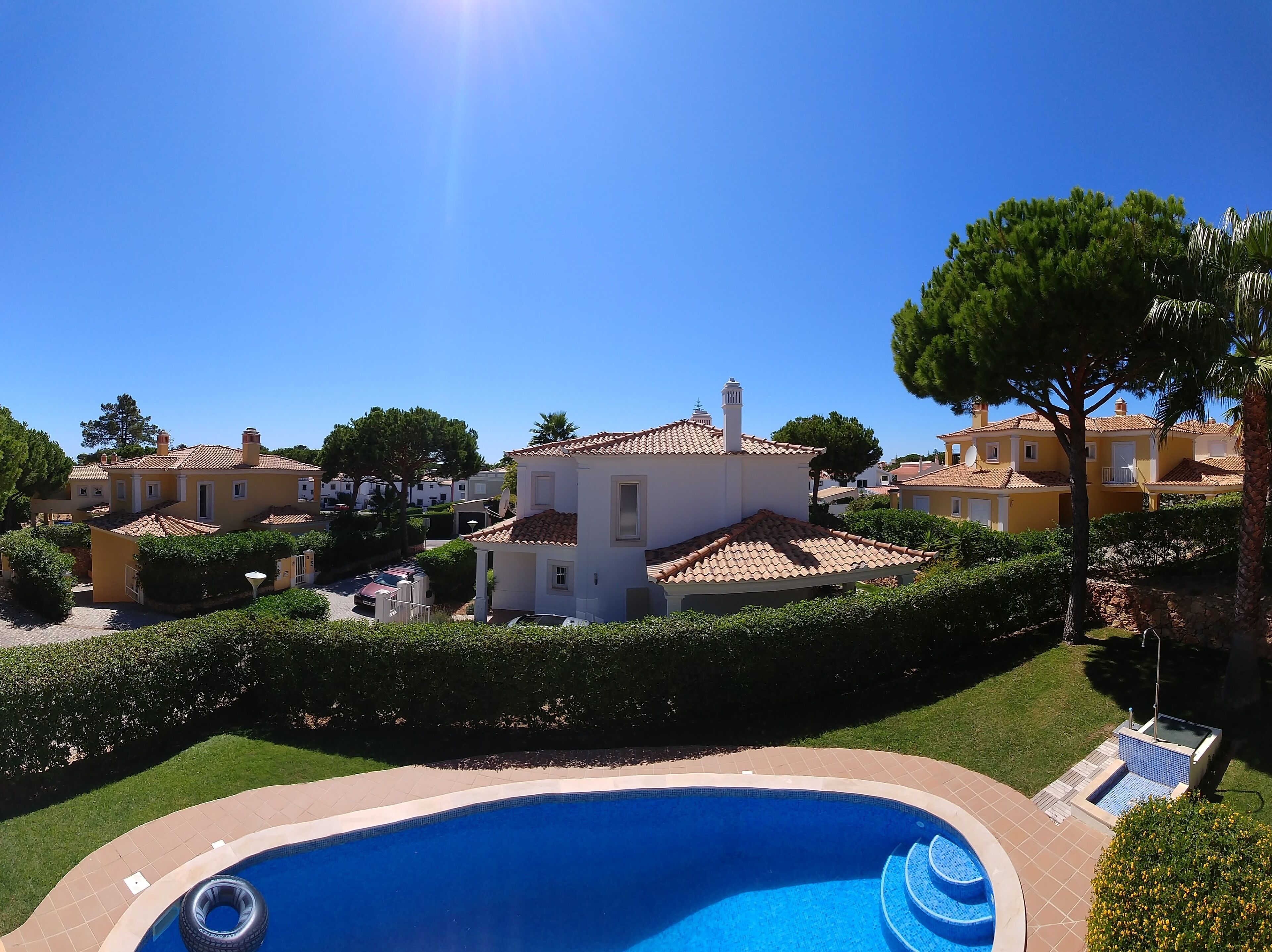 A residential area with a swimming pool, houses with tiled roofs, and a clear blue sky.
