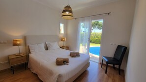 A bedroom with a large bed, two bedside lamps, a chair, and a view of a swimming pool. - Very nice house fully equipped, wonderful terrace with garden, garage (VILAMOURA)
