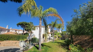 A white building with a tiled roof, surrounded by a well-maintained garden with palm trees and other greenery. - Very nice house fully equipped, wonderful terrace with garden, garage (VILAMOURA)